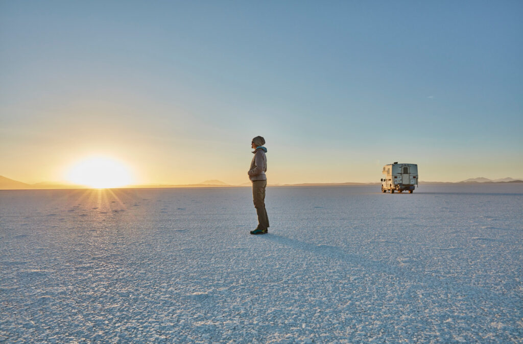 Bolivia, Salar de Uyuni, woman standing at camper on salt lake at sunset